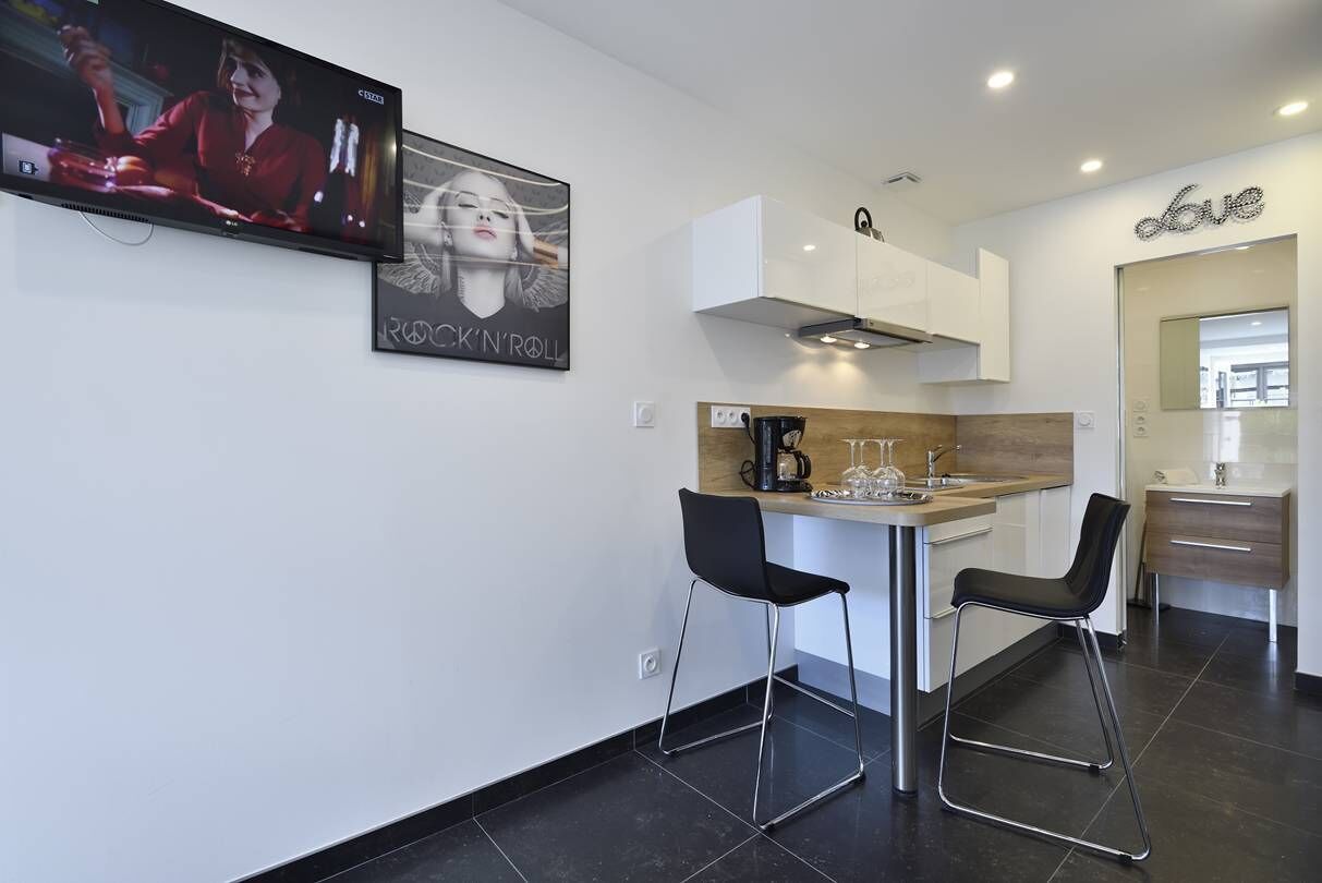 Een moderne keuken met een televisie, een koffieapparaat en twee barkrukken.