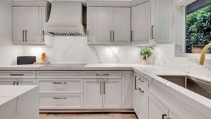Una cocina moderna con armarios blancos, encimera de mármol y estufa integrada.