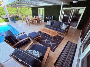 Ein überdachter Patio-Bereich mit Pool, Gartenmöbeln und Blick ins Grüne.