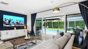 Un salón moderno con televisor, sofá, mesa de centro y vistas a una piscina y jardín.