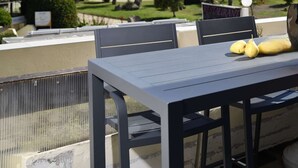 Um terraço com mesa e cadeiras, com vista para uma área arborizada e edifícios.