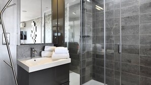 Uma casa de banho moderna com cabine de duche em vidro, lavatório com espelho e porta-toalhas.