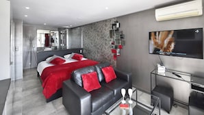 Quarto de hotel moderno com cama, sofá, televisão e ar condicionado.