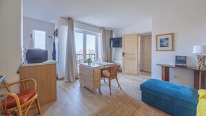 A room with a wooden desk, a chair, a television, a sofa, and a window with curtains. - Le Nid de Cabourg - Welkeys (Cabourg)