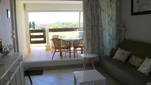 Un soggiorno con divano, un tavolino, un tavolo da pranzo con sedie e una vista su un balcone esterno attraverso una porta scorrevole.