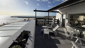 A patio with outdoor seating, a view of the ocean, and a building with large windows. - LA BELLE VUE - Studio Port Nature Studio 115s with garage - Luxe - Seafront - 2 people (AGDE)
