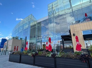 A modern building with large glass windows, a sign for 'ERIN MILLS TOWN CENTER,' and outdoor seating with red umbrellas.