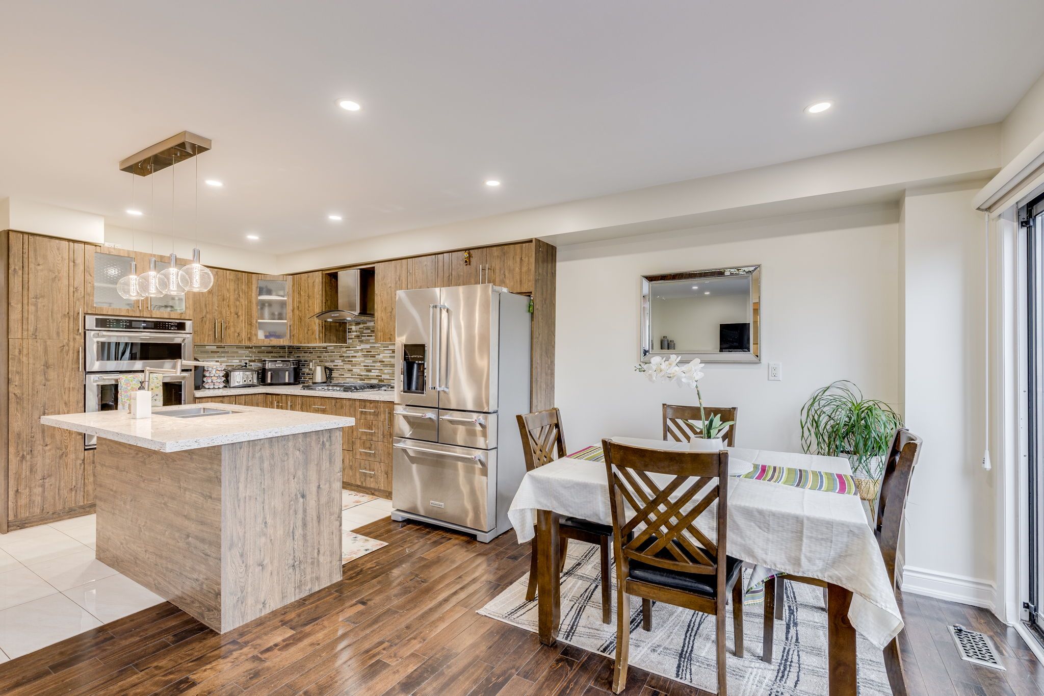 A modern kitchen with a central island, stainless steel appliances, wooden cabinets, and a dining area with a table and chairs.