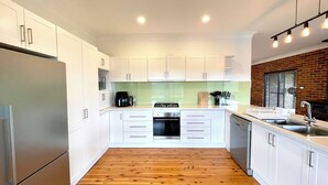 A modern kitchen with white cabinets, a wooden floor, a gas stove, a dishwasher, and a brick wall.