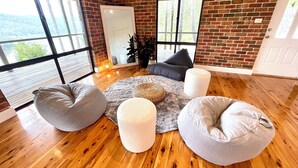 A room with a brick wall, large windows, a wooden floor, and a seating area with bean bags and a rug.