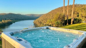 A hot tub with a river view, surrounded by greenery and hills.