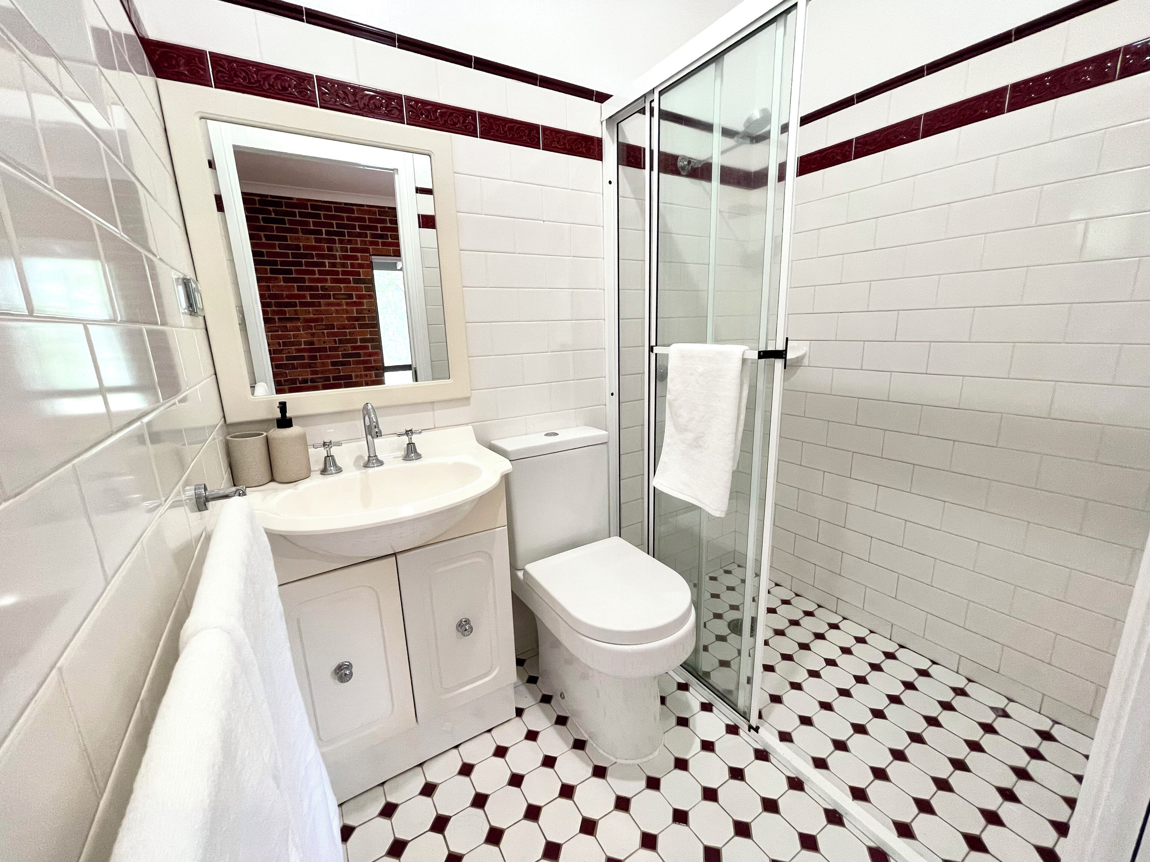 A bathroom with a white sink, a toilet, a glass shower enclosure, and a mirror above the sink.