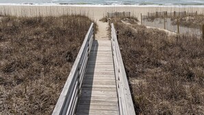 Ein hölzerner Steg führt zu einem Strand, begleitet von einer Umzäunung.