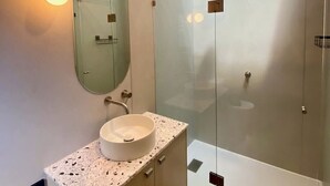 Ett modernt badrum med en duschavdelning med glasväggar, en rund spegel och ett handfat i granit.