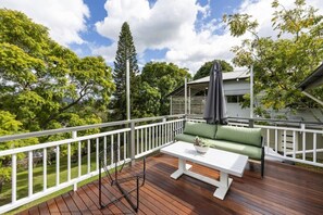 Una terraza con barandilla blanca, un sofá verde, una mesa blanca y un paraguas gris.
