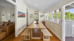 Une pièce spacieuse avec une longue table en bois, des bancs, un canapé et de grandes fenêtres donnant sur un paysage verdoyant.