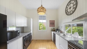 Une cuisine moderne équipée d’un lave-linge, d’une grande horloge et d’une fenêtre donnant sur un paysage verdoyant.