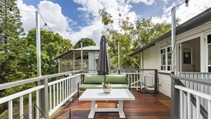 Une terrasse en bois avec une balustrade blanche, un canapé vert et une table blanche.