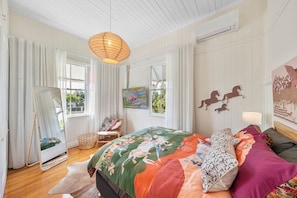 Un dormitorio con una cama grande, un espejo de pie, una silla y obras de arte en las paredes.