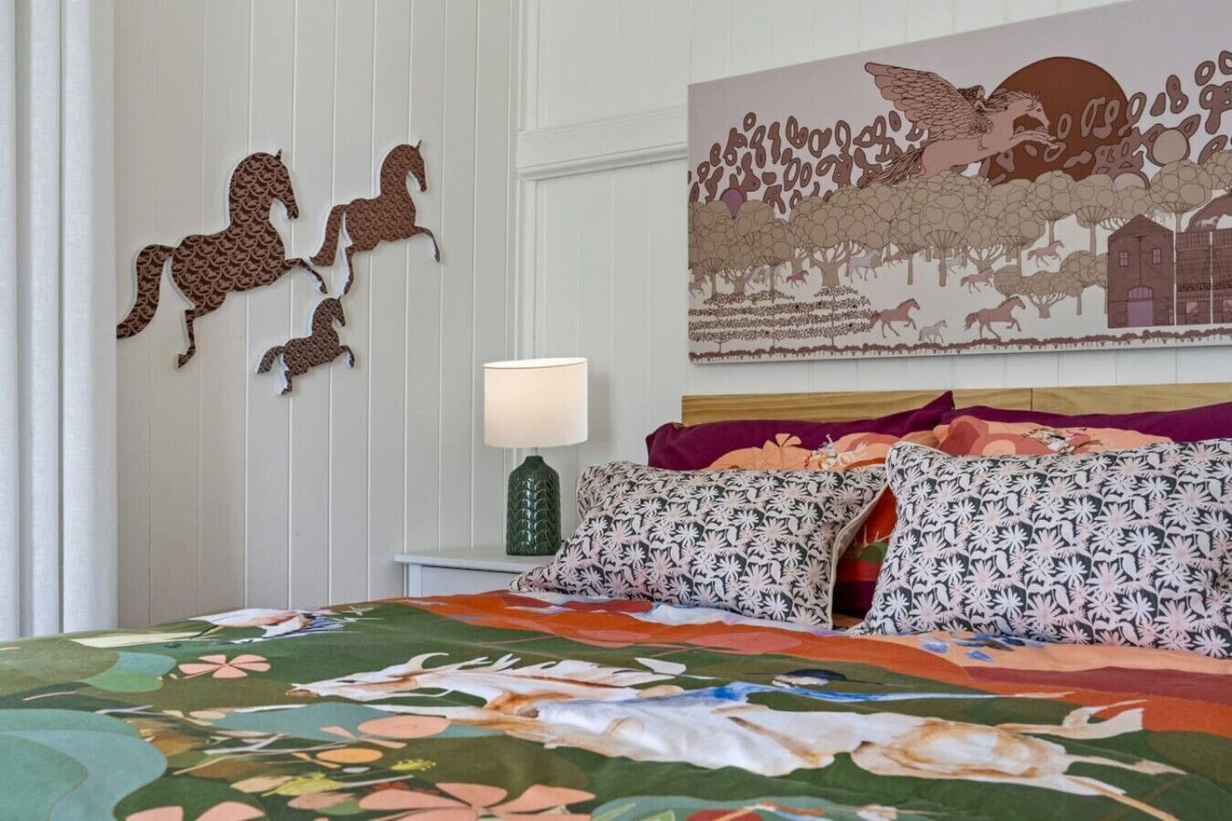A bedroom with a bed, pillows, a wall-mounted lamp, and decorative horse cutouts.