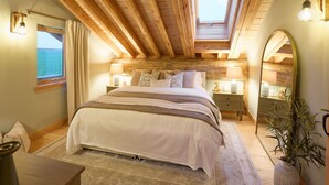 A bedroom with a large bed, a skylight, a bedside table with a lamp, a mirror, and a view of the sea. - Host Stay Cabin on the Loch (Kelso)