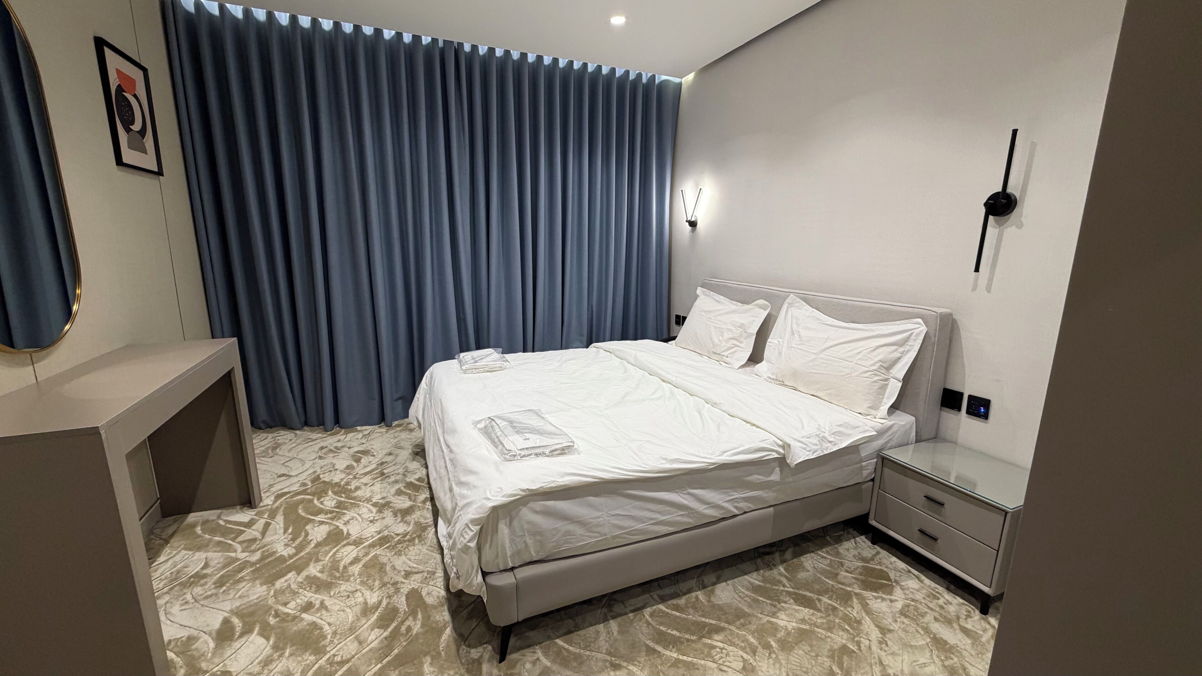 Ein modernes Schlafzimmer mit Bett, Nachttischen, einer Wandleuchte und einem großen Fenster mit Vorhängen.