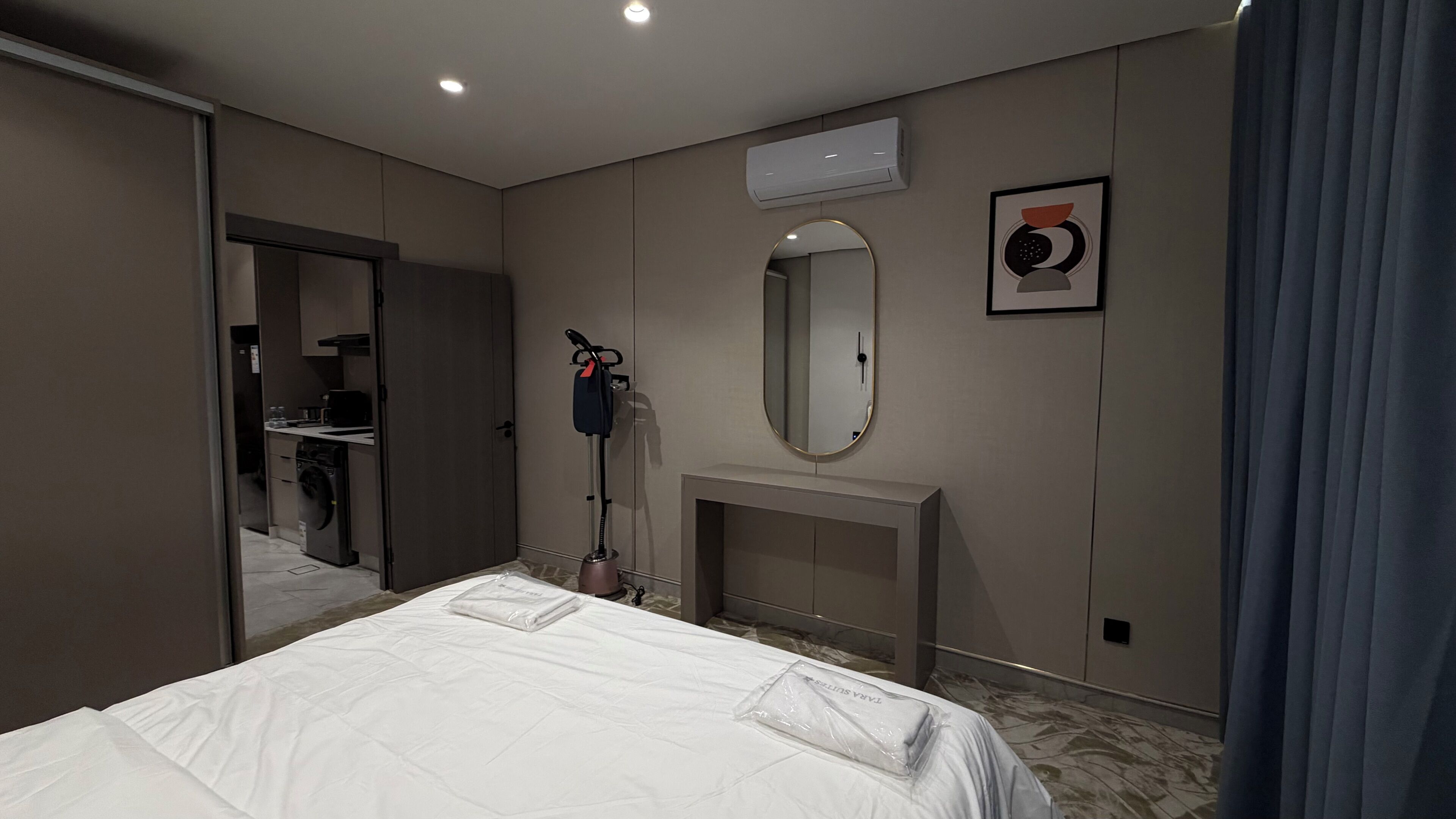 A hotel room with a bed, a mirror, a fireplace, an air conditioning unit, and a bathroom visible through an open door.