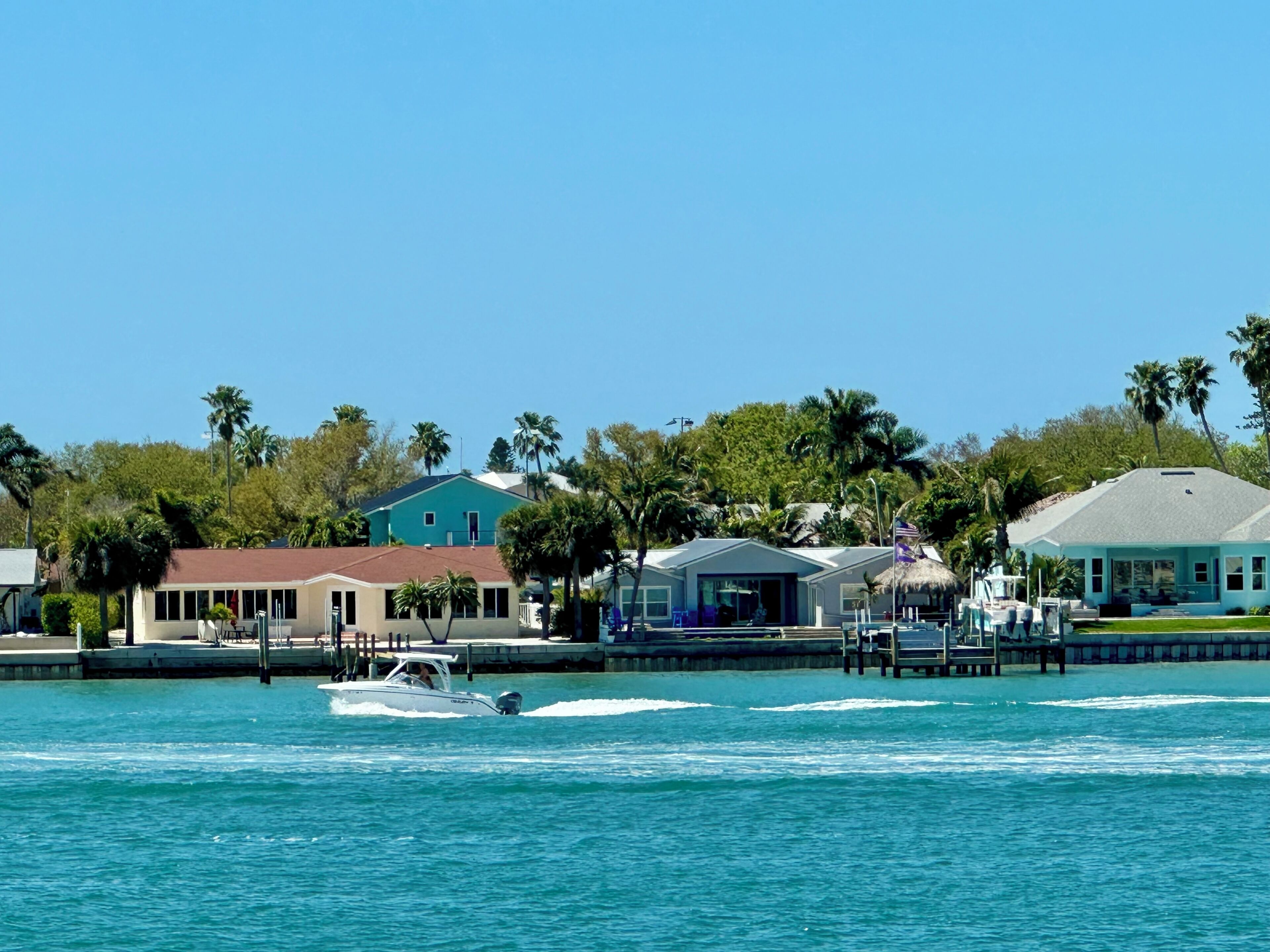 A waterfront property with a boat dock, a house with a blue roof, and palm trees.