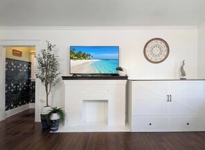 A living room with a fireplace, a television, a cabinet, and a decorative wall piece. - CozyVibeStay. Walk to Sand. Workspace. Parking (Long Beach)