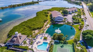 Vista aerea di un resort con una grande piscina, un campo da tennis e un porto turistico.