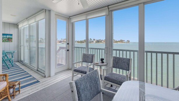 Un balcone coperto con vista sul mare, sedie in vimini, un tavolino e una ventola a soffitto.