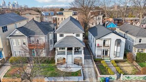 A residential area with houses, a central building with a balcony, and a city skyline in the background. - New 8bd 7.5ba 6,600 sq ft Home in O4W Inman Park WALKABLE ATL Eastside Beltline (Atlanta)