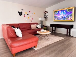 Ein Wohnzimmer mit einem roten Sofa, einem Couchtisch, einem Fernseher und Wanddekorationen, darunter Mickey Mouse Ohren und ein Gemälde einer Burg.
