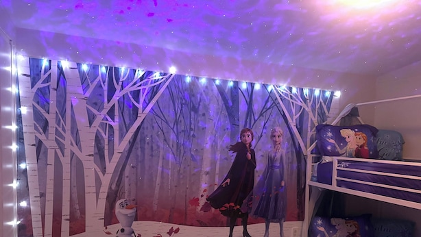 Una habitación con literas, un mural en la pared y un techo con proyecciones de estrellas.