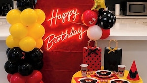 Una cocina con armarios blancos, un arco de globos rojos y una mesa decorada con motivos de Mickey Mouse.
