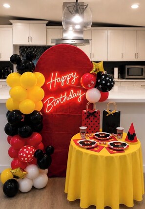A kitchen with white cabinets, a red balloon arch, and a table with Mickey Mouse-themed items.
