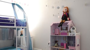 Una habitación infantil con literas, una casa de muñecas y una pared decorada con estrellas.
