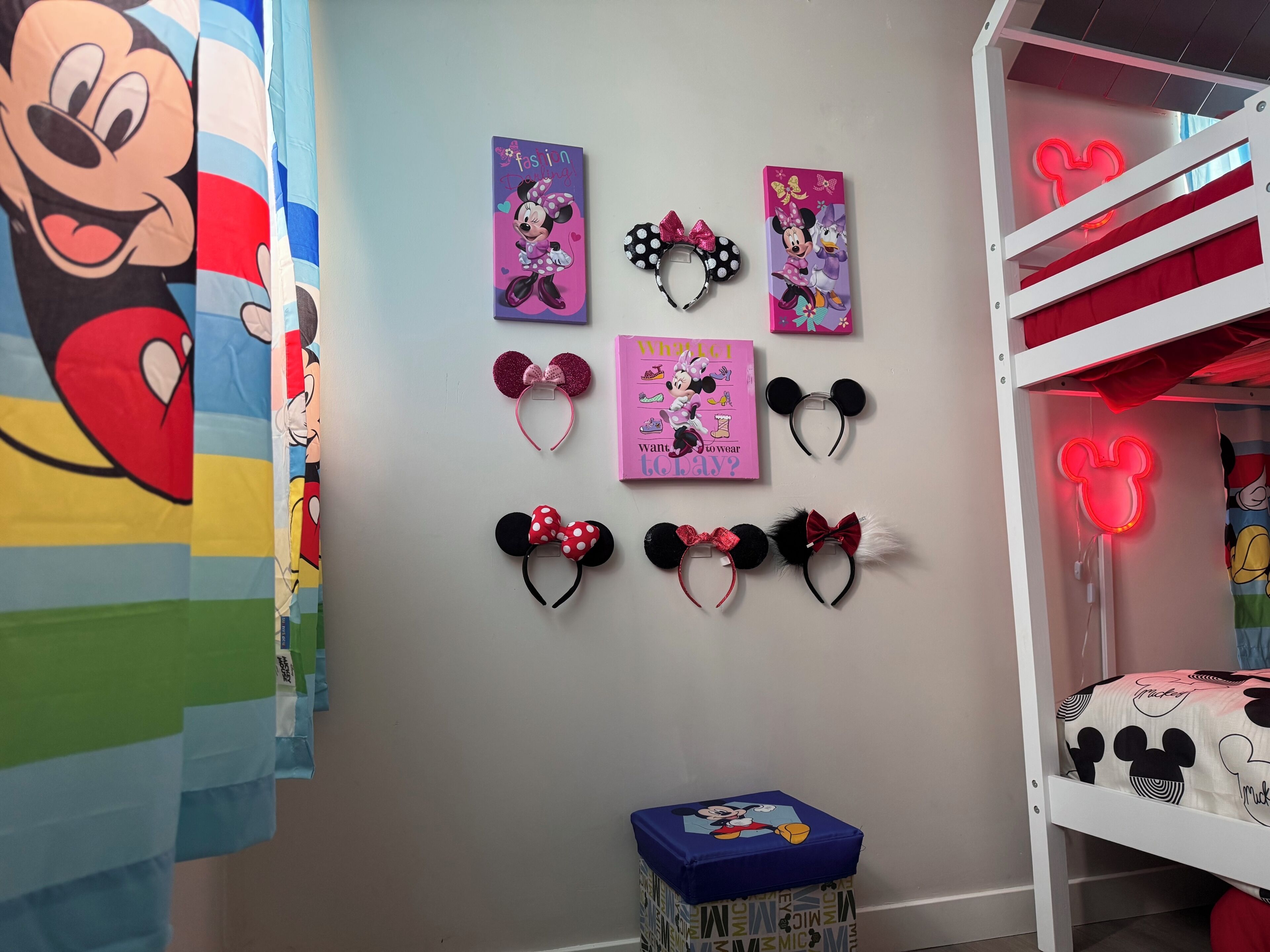 Una habitación infantil con literas, diademas de Minnie Mouse, un libro titulado '¿Qué quiero vestir hoy?' y un letrero de neón de Mickey Mouse.