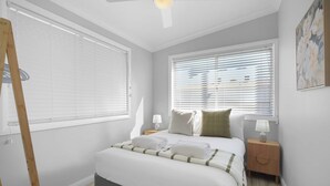 A bedroom with a bed, bedside tables, a ceiling fan, and a window with blinds.