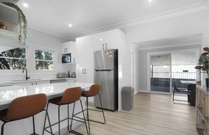 A modern kitchen with white cabinets, a stainless steel refrigerator, and a bar area with stools.