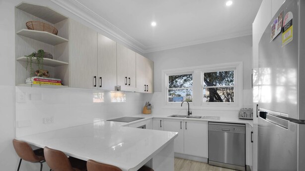 A modern kitchen with white cabinetry, a central island with bar stools, a stainless steel dishwasher, and a refrigerator.