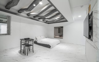 A modern bedroom with a bed, a desk with chairs, a TV, and a bathroom mirror.