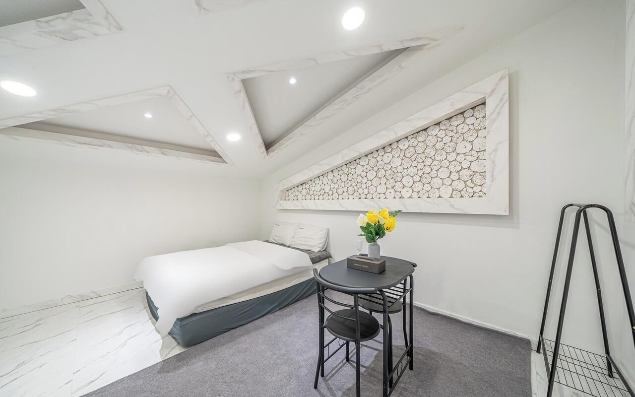A modern room with a bed, a small table with a vase of flowers, a wall art piece, and a ceiling with recessed lighting.