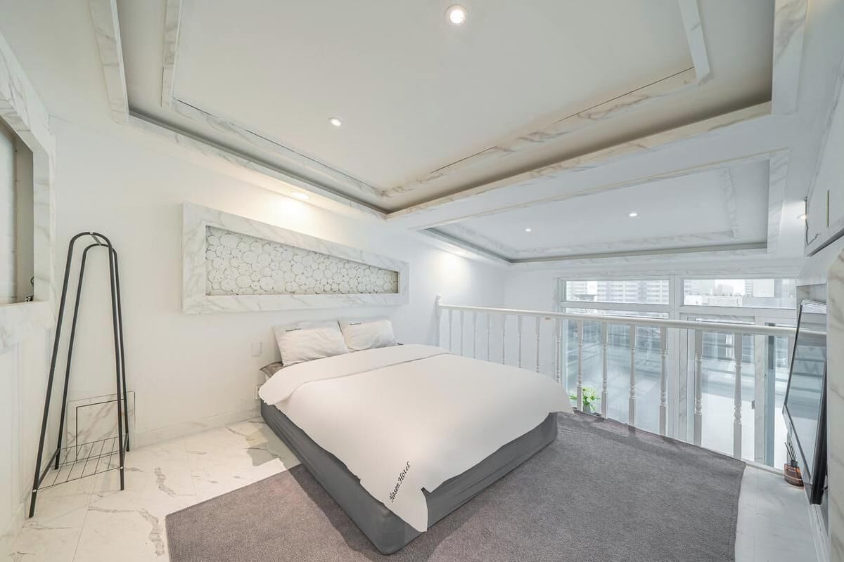 A modern bedroom with a large bed, a marble wall, and a balcony with a city view.