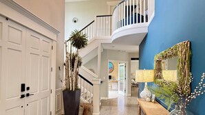 A spacious foyer with a grand staircase, a large potted plant, a console table with decorative items, and a blue accent wall. - Beautiful Eastside 5 bedroom resort like home with Hot-tub and AC (Newcastle)