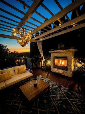 Une terrasse extérieure avec une cheminée en pierre, un canapé en bois et un tapis à motifs.