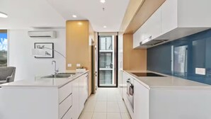 A modern kitchen with white cabinetry, a central island, and a view through a glass door. - 2BR Contemporary Comfort in Belconnen (Belconnen)