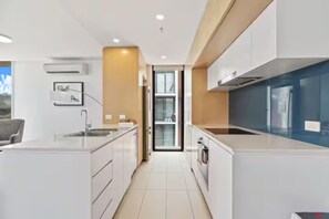 Cozinha moderna com armários brancos, uma ilha central e vista através de uma porta de vidro.