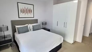 A modern bedroom with a large bed, a nightstand with a lamp, a wardrobe, and a framed artwork on the wall. - 2BR Contemporary Comfort in Belconnen (Belconnen)