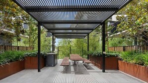 An outdoor patio with a wooden table and benches, surrounded by planters and a metal pergola structure. - 2BR Contemporary Comfort in Belconnen (Belconnen)